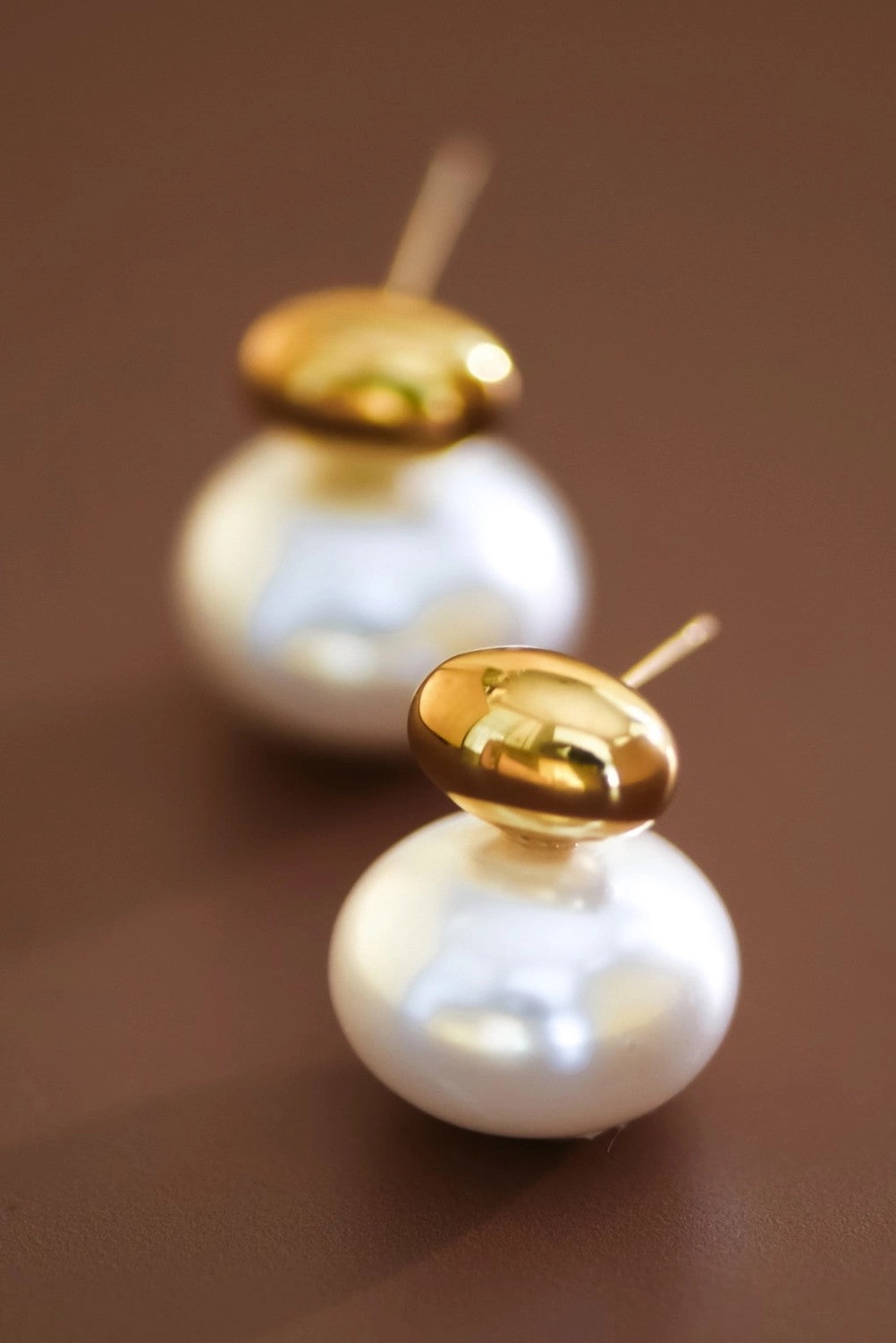 Gold and pearl stud earrings on a warm brown backdrop