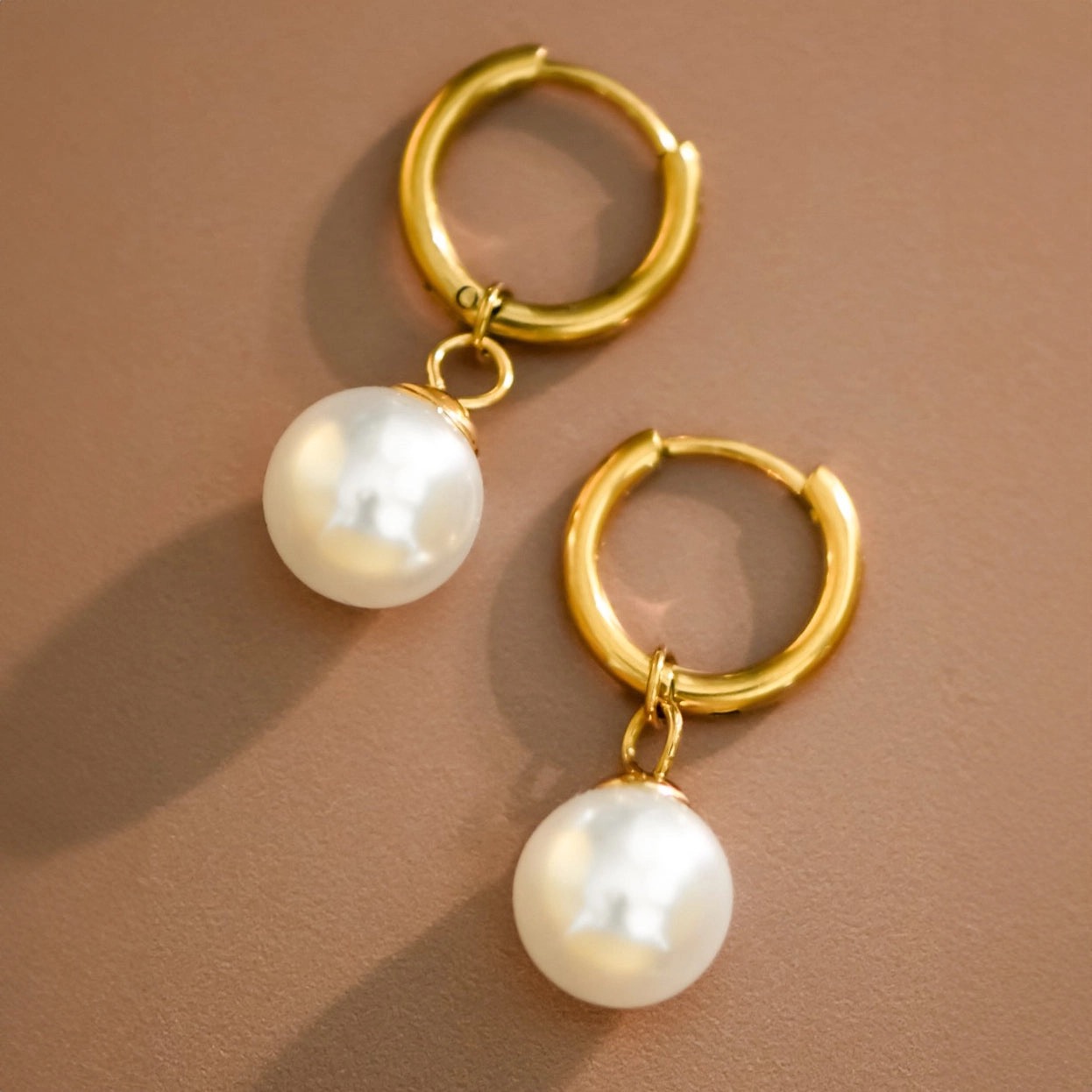 Gold huggie hoop earrings with pearl drops on a warm brown backdrop